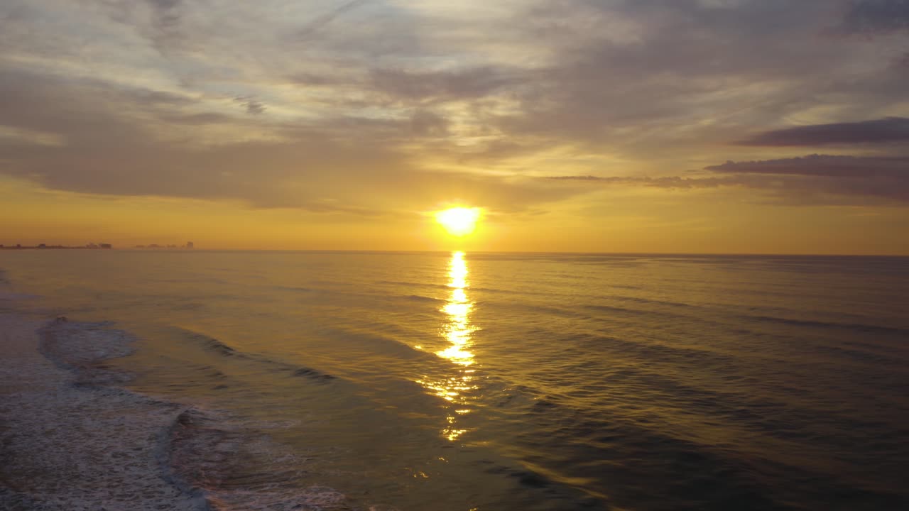 Stationary wide shot of brilliant yellow cloudy sunset over ocean with small rolling waves