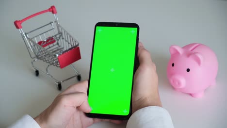 teléfono con una pantalla chromakey en las manos de un primer plano. vista superior de la caja de ahorros del teléfono inteligente y el carrito de compras copia el espacio sobre fondo blanco