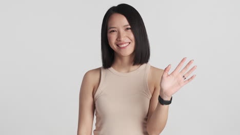 asian woman smiling and waving hello on camera.