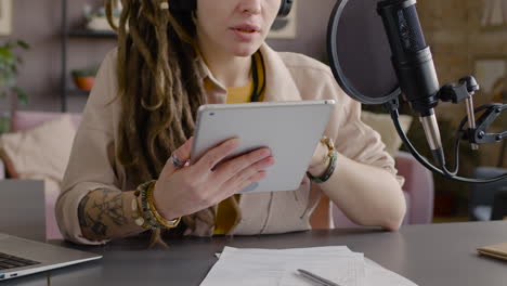 vista ravvicinata di una donna irriconoscibile con dreadlocks che registra un podcast che parla in un microfono seduto alla scrivania con laptop e documenti