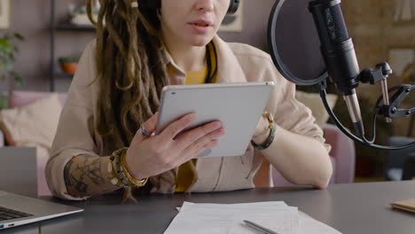 vista de cerca de una mujer irreconocible con rastas grabando un podcast hablando en un micrófono sentado en el escritorio con una computadora portátil y documentos