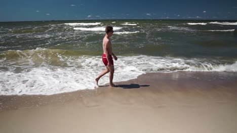 young man in red shorts walks in a beach by the sea