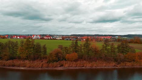 un drone survole la rive d'un lac il y a un pré vert une petite ville et un ciel bleu nuageux