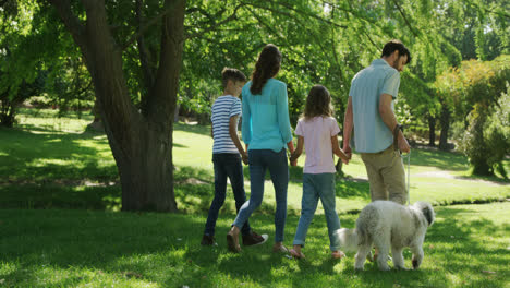 family walking with their dog in the park on a sunny day