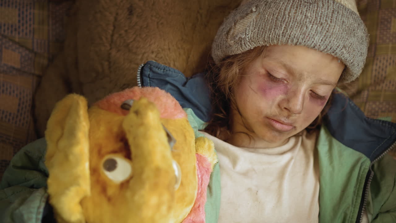 Aerial view of exhausted displaced child with bruised eyes and dirty face, sleeping in ragged clothes, clutching worn yellow stuffed toy, capturing sorrow and poverty