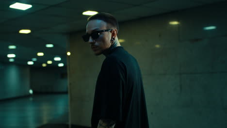 man with tattoos and glasses in a dimly lit urban setting