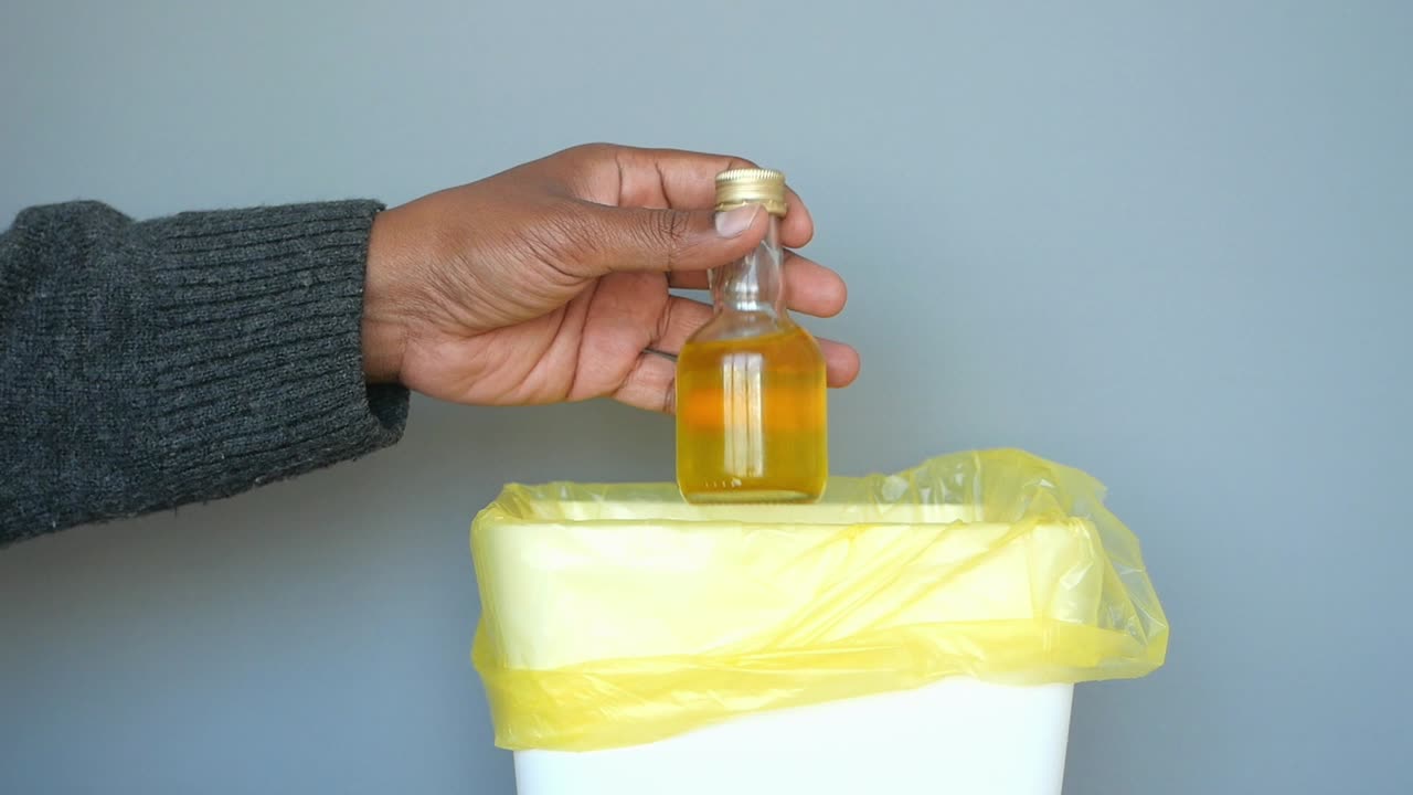 mano tirando una pequeña botella en un contenedor de basura