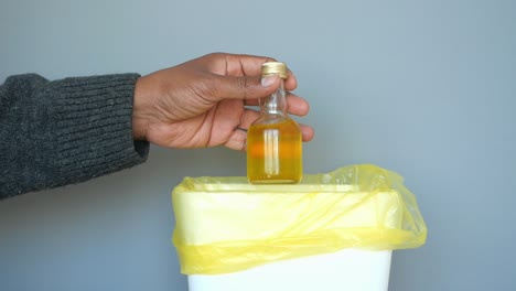 mano tirando una pequeña botella en un contenedor de basura