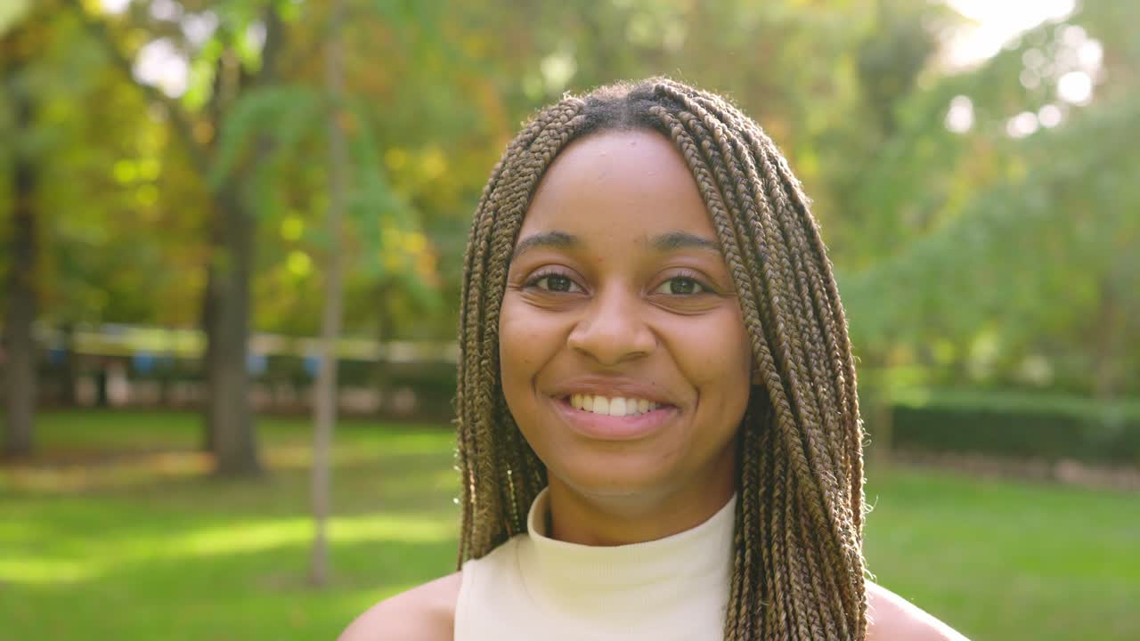 Close-up of a happy Black woman with braids smiling in a sunny park
