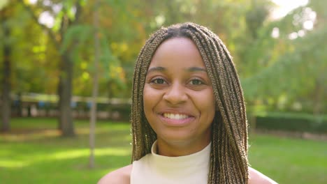 close-up of a happy black woman with braids smiling in a sunny park