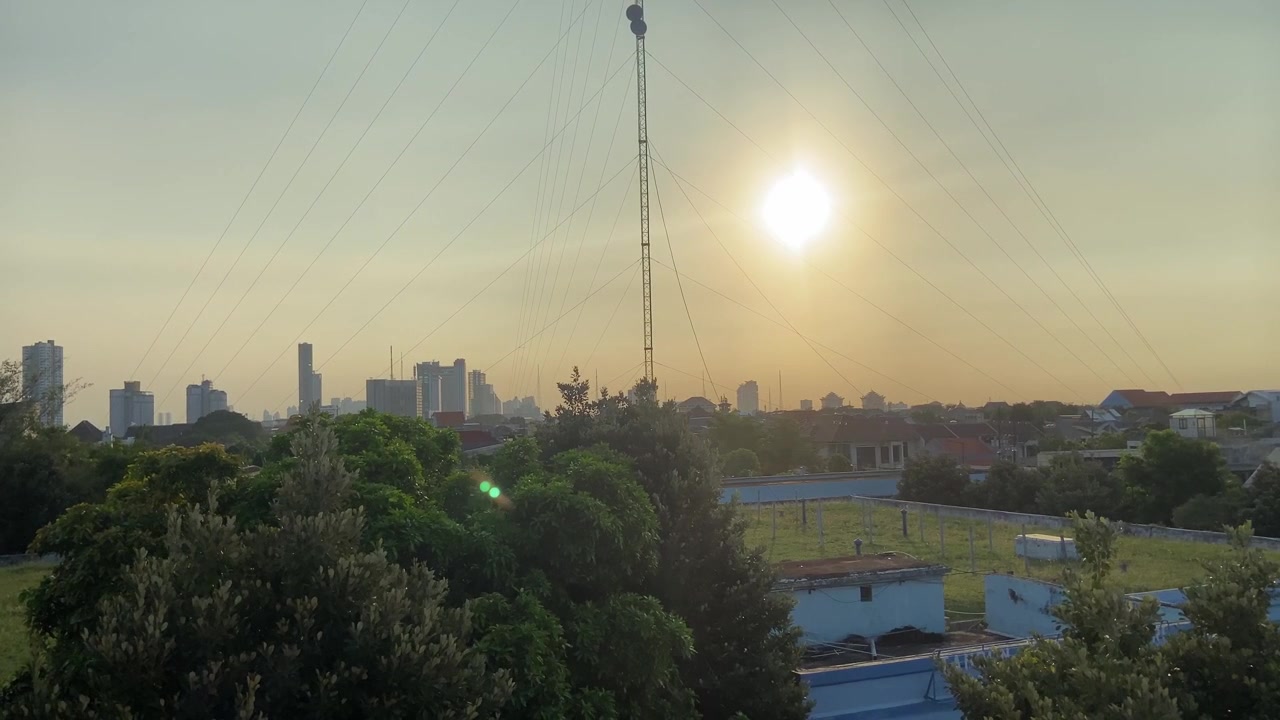 Pôr do sol dourado sobre o horizonte da cidade com torre de comunicação e árvores verdes