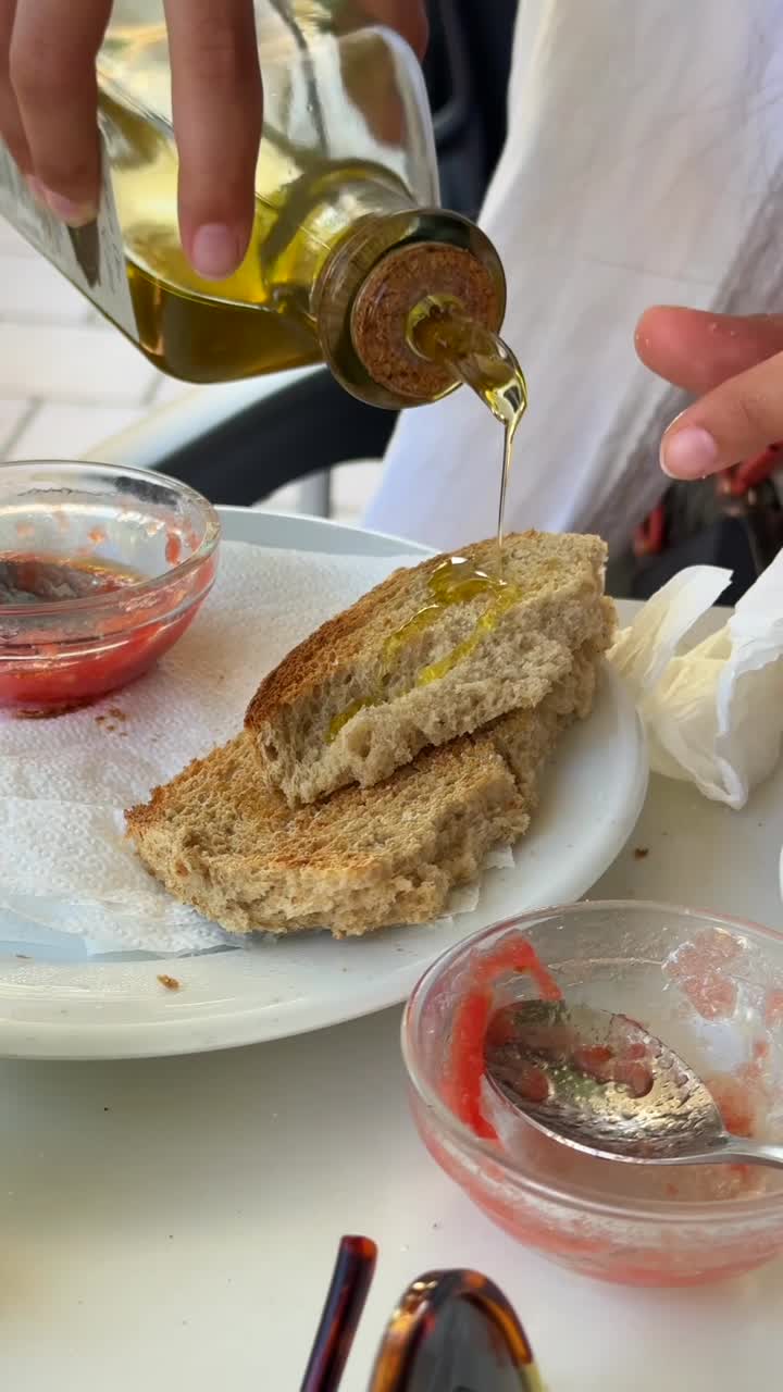 Primo piano di mani che preparano una bruschetta con olio d'oliva e pomodoro.