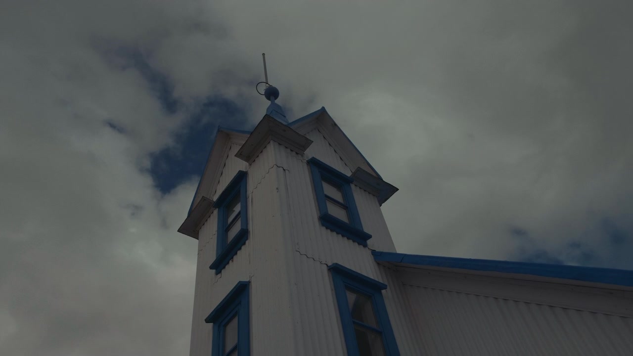 Campanile storico bianco con dettagli blu sotto un cielo nuvoloso e suggestivo