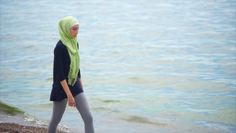 young woman in hijab walking on the beach