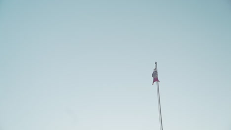 a flag windsock waves in the breeze on a flagpole against a clear blue sky still shot