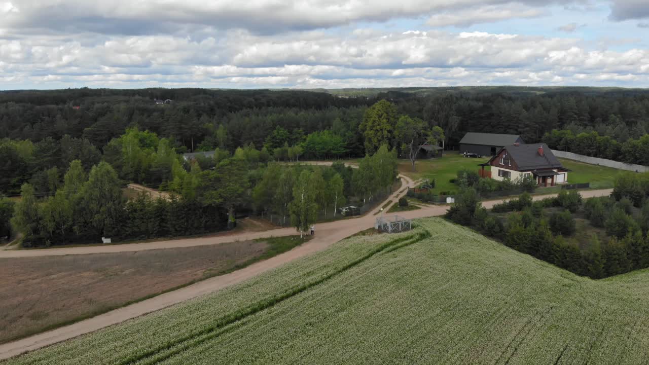 Aerial view of a lush green field and forest with a small, gray-roofed house in the distance