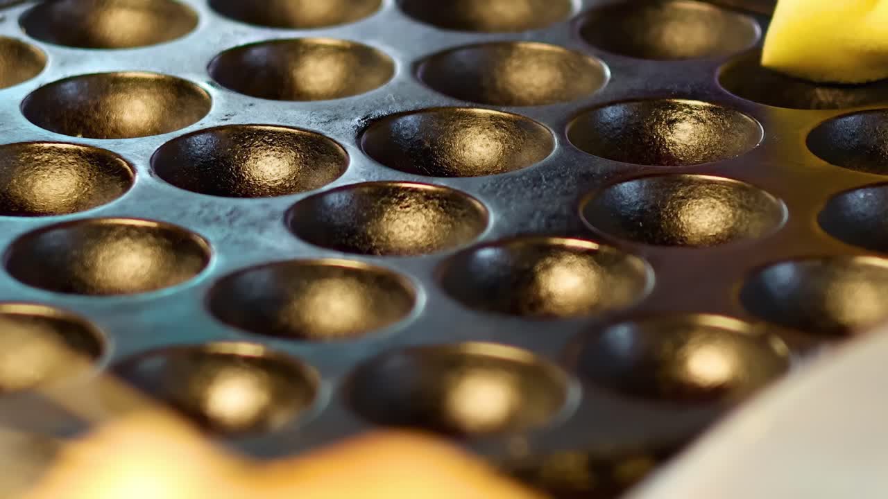 Hands cleaning a cast iron mold with a cloth, preparing it for cooking.