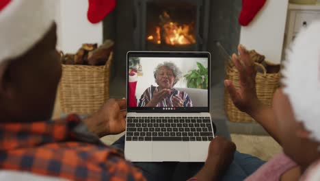 pareja afroamericana usando una computadora portátil para una videollamada de navidad con una familia sonriente en la pantalla