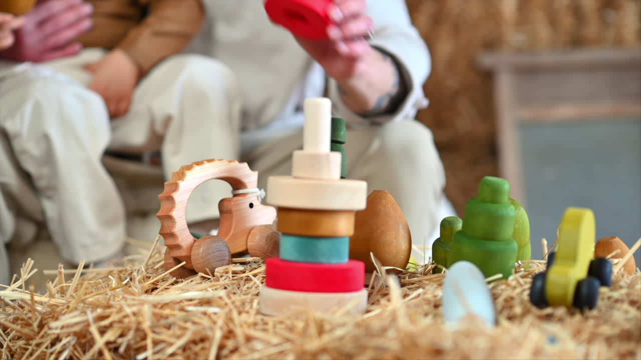 Father playing with his son with colourful, ecological wooden toys in a barn, near square hay bales