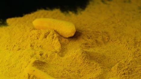 peeled turmeric root falls on heap of turmeric powder