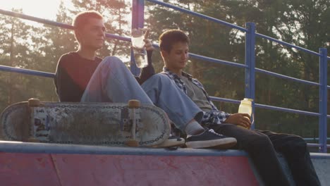 Zwei-Freunde-Sitzen-Im-Skatepark-Und-Unterhalten-Sich,-Während-Sie-Wasser-Trinken-1