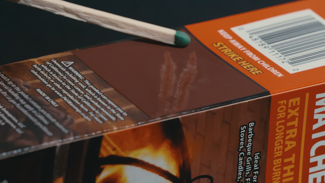 Long, green tipped match stick striking matchbox and igniting a flame in slow motion