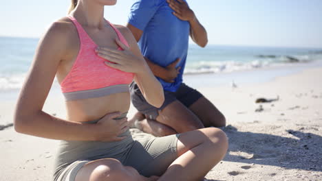 young caucasian woman and biracial man meditate on a sunny beach