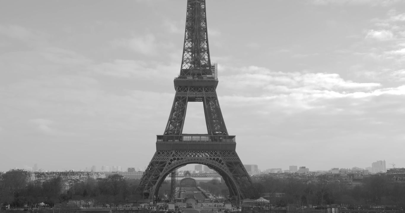 Ripresa in bianco e nero con panoramica verso il basso della Torre Eiffel con traffico in movimento sotto a Parigi, Francia, in una giornata nuvolosa