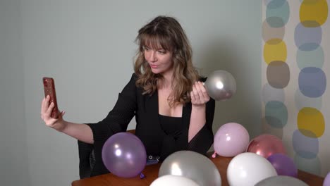 mujer joven sentada en una mesa, tomándose un selfie rodeada de globos