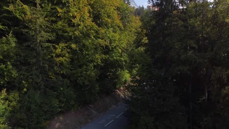 Drone-going-up-revealing-a-tall-buildin-in-the-middle-of-a-pine-forest,-mountain-range-and-nice-autumn-colors