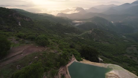 hermosa toma aérea de drones del acantilado y el cuerpo de agua sobre las montañas con el atardecer y las colinas brumosas en la distancia