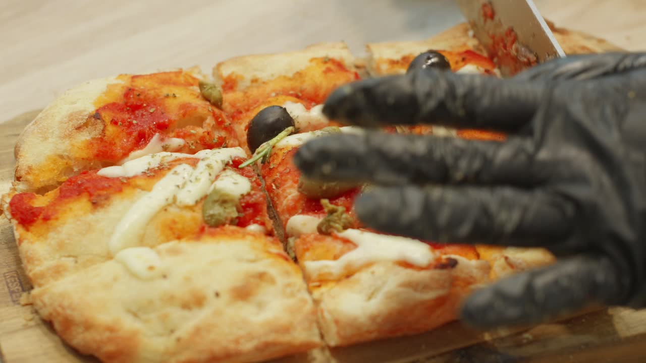 Close-up on a freshly baked focaccia pizza being sliced with olives and cheese toppings in a professional kitchen.