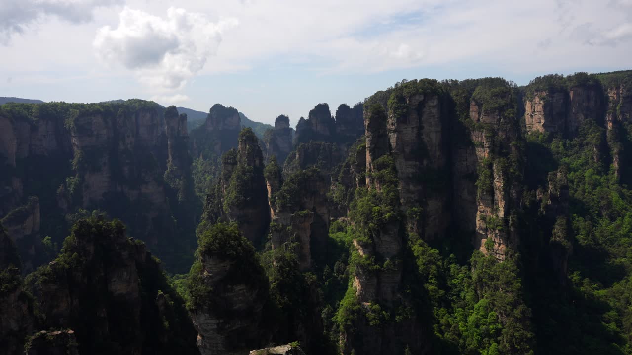 Tilt down view of the famous sandstone pillars in China reveals lush green vegetation at the mountain base