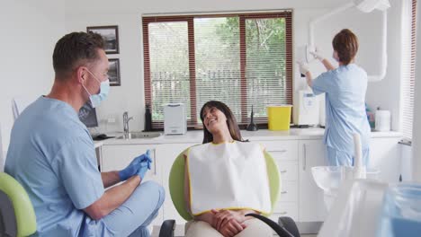 caucasian male dentist with face mask preparing smiling female patient at modern dental clinic