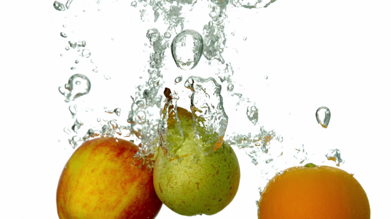 Pera, mela e arancia che si tuffano nell'acqua su sfondo bianco
