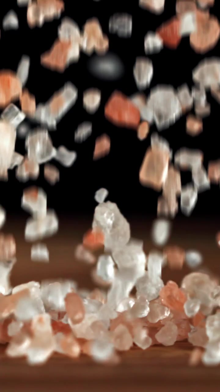 Sale rosa dell'Himalaya grosso e cristalli di sale bianco che cadono su una superficie di legno