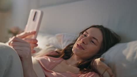 closeup relaxed girl videocalling in bed. positive awake woman holding mobile