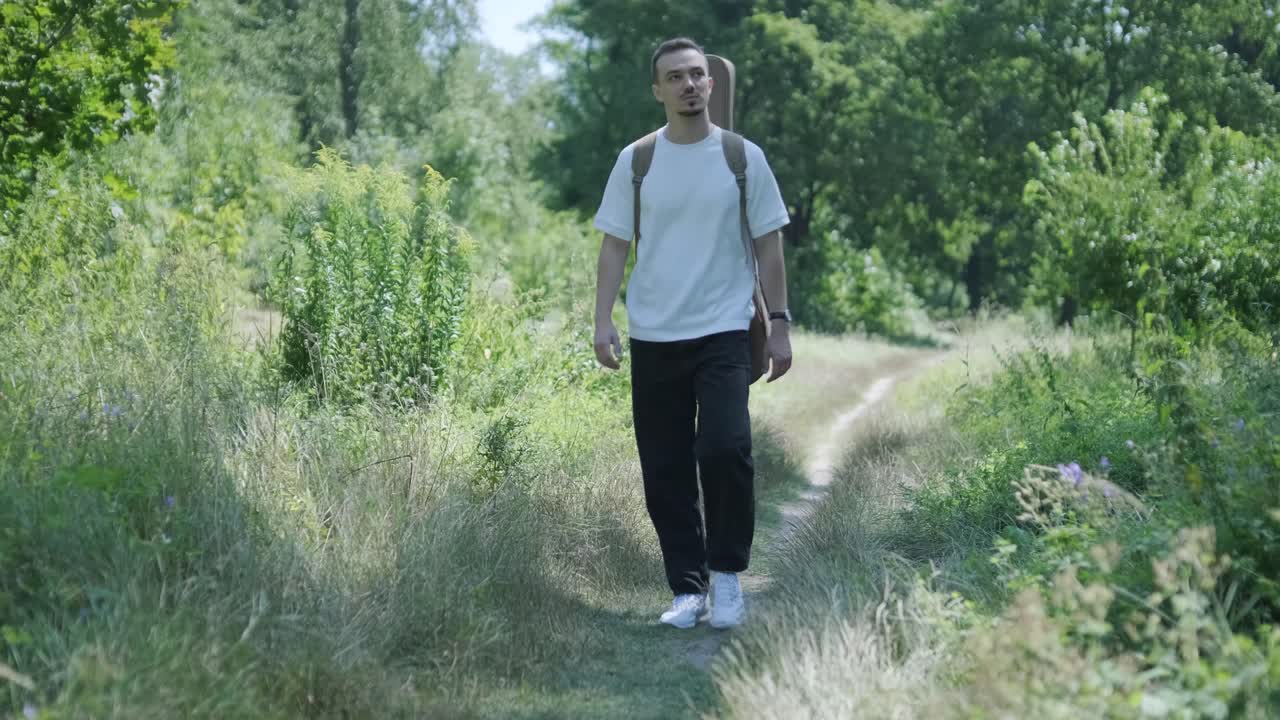 Junger Mann geht mit Gitarre auf der Straße nahe Wald