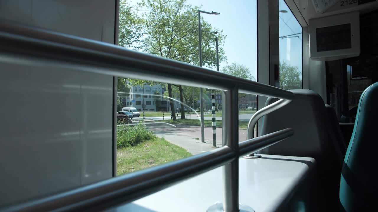 View from tram window passing through Kralingse Bos in Rotterdam Netherlands showing interior metal railings and lush green trees outside creating peaceful urban transport atmosphere