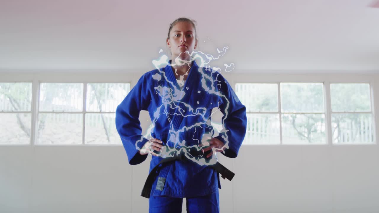 Female martial-arts student walking center on mats, stopping, activating torso energy for training