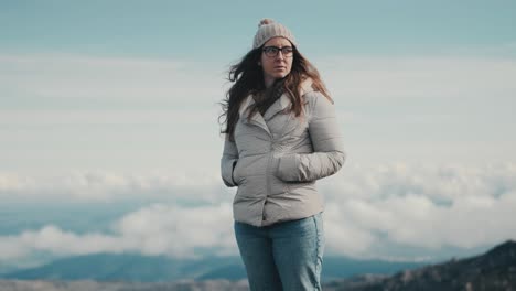 Medium-shot-of-a-young-woman-admiring-the-stunning-landscape-of-mountains-and-clouds-on-the-horizon-while-enjoying-the-beauty-of-nature-in-the-mountains