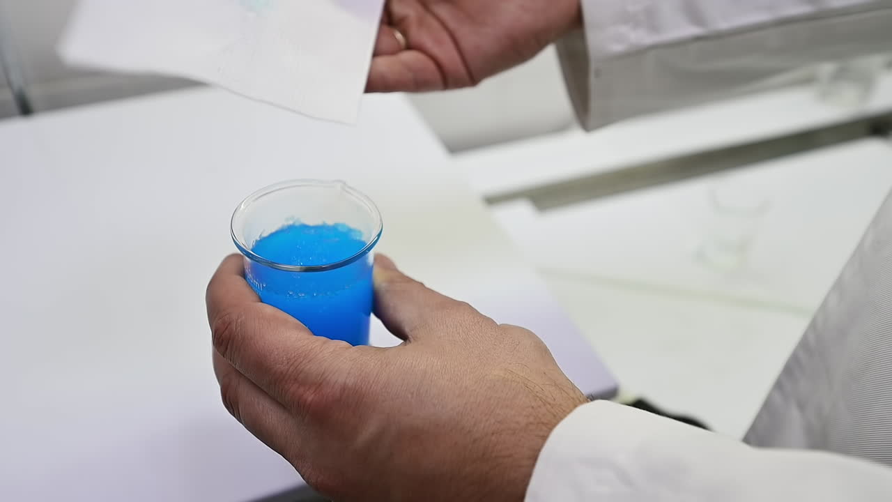 Male hand holding a beaker with blue staff from inside the diaper. Researcher testing the absorption with the help of a napkin. Close up.
