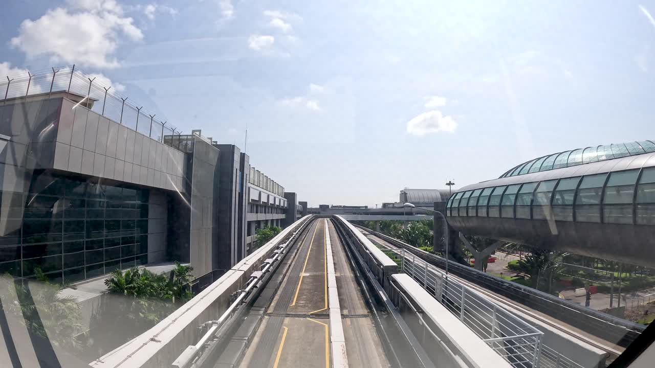 Forward-facing view from skytrain moving through glass terminal buildings in bright daylight, steady camera