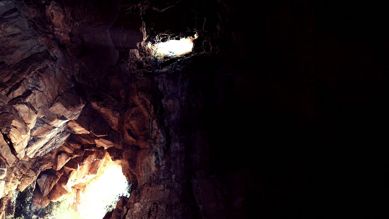 Majestic light streaming through rocky cave openings in a dark cavern