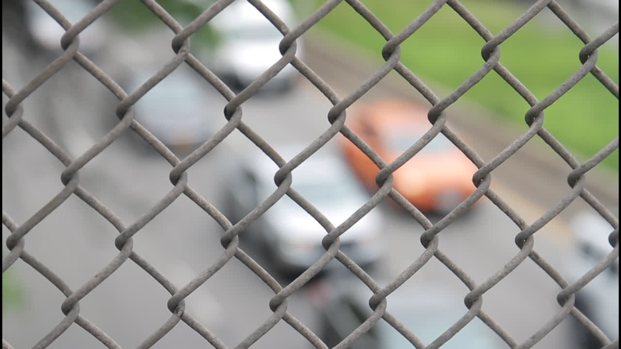 Blurry view of traffic through a chain link fence