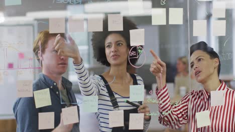 diverse male and female business colleagues discussing by glass wall with memo notes