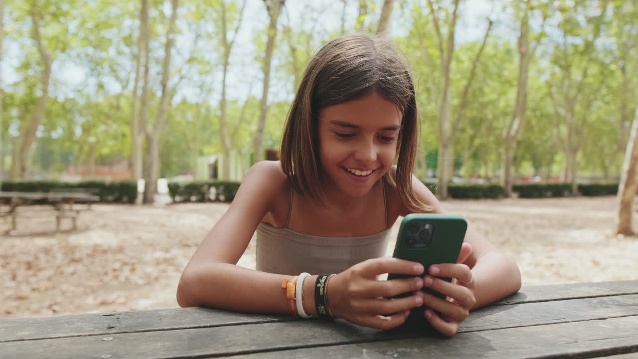 Happy Young Girl Using Smartphone at a Picnic Table in a Park