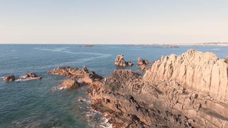 Reveal-drone-footage-of-rocky-outcrop-with-crystal-clear-sea-on-bright-sunny-day-in-Guernsey