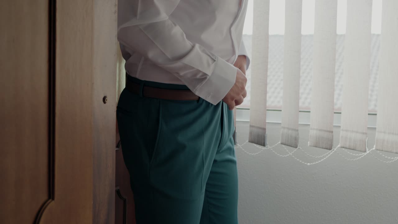 Groom adjusting his teal trousers and belt, preparing for the wedding ceremony
