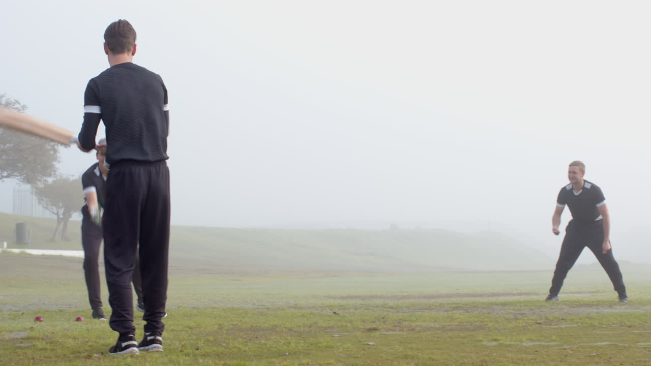 Playing cricket, man swinging bat on foggy field, practicing batting skills
